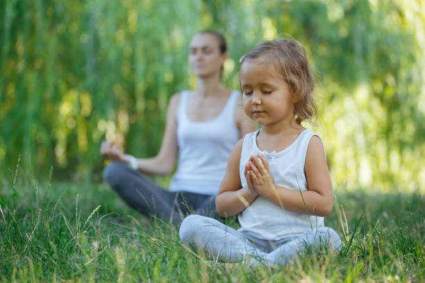 Young mother and cute little daughter meditating in lotus pose together stock photo
