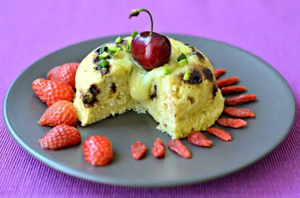 Two chocolates bowlcake: chunky dark chocolate chips with a melting white chocolate and macadamia filling. Topped with goji, pistachio, cherry and raspberry. Dark plate, purple background