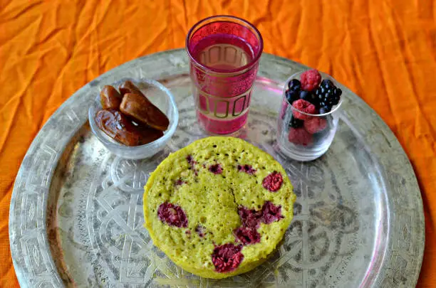 Pistachio, raspberry and white chocolate bowlcake with dates, berries and tea on Moroccan silver plate
