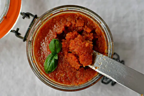 Sun-dried tomato and almond pesto - Pesto rosso sauce in a jar with knife, top view