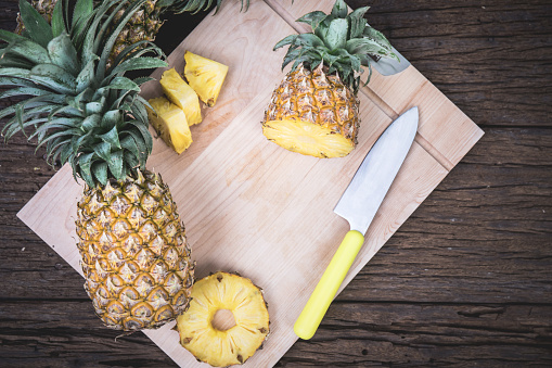 Sliced pineapple on a cutting Board with a knife. On a wooden table.