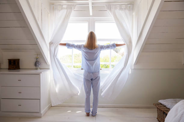 vista posteriore della donna che apre le tende e guarda fuori dal finestrino - curtain window women opening foto e immagini stock