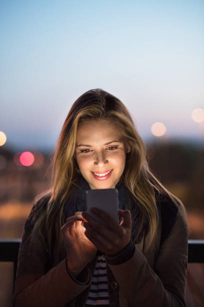 Woman in the city at night holding smartphone, texting. Beautiful woman in the city at night holding smartphone, texting. mobile phone lights up stock pictures, royalty-free photos & images