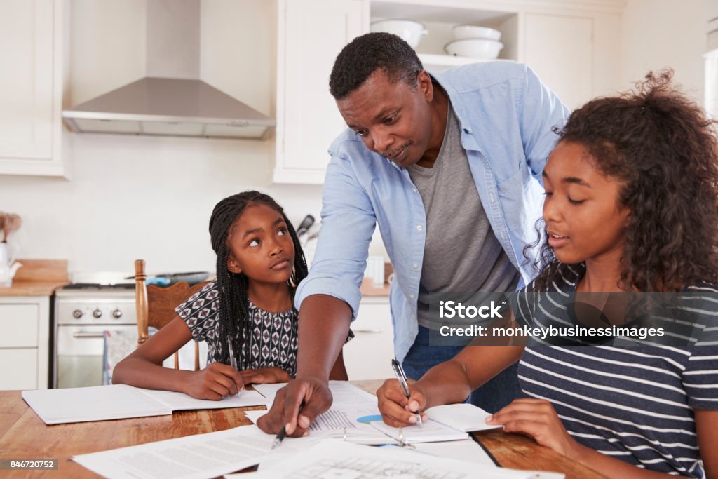 Father Helping Two Daughters Sitting At Table Doing Homework Teenager Stock Photo