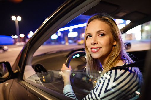 Beautiful young woman in a city driving her modern car at night.