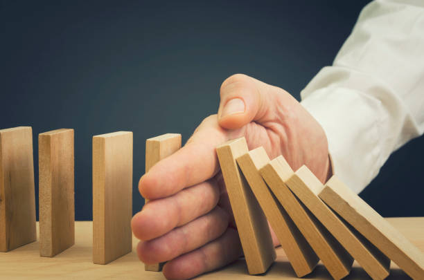 Businessman Stop Domino Effect Businessman halting the domino effect inserting his hand between falling and upright wooden blocks inconvenience photos stock pictures, royalty-free photos & images