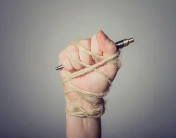 Hand with pen tied with rope, depicting the idea of freedom of the press or freedom of expression