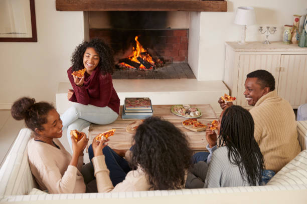 istock Family Sitting On Sofa In Lounge Next To Open Fire Eating Pizza 846735214