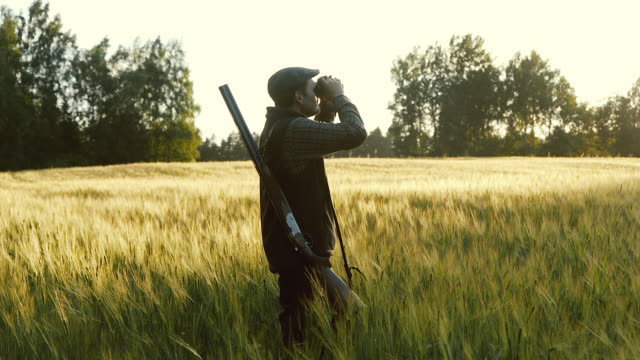 Hunter rises binoculars at golden hour (slow motion)
