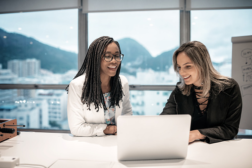 two young brazilian businesswoman with laptop communicating in office in Rio de Janeiro