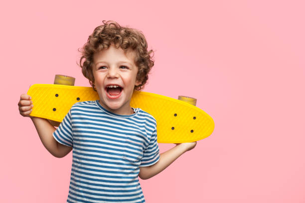 Cheerful boy with yellow longboard Charming curly boy holding yellow longboard and looking away on pink background. charming photos stock pictures, royalty-free photos & images