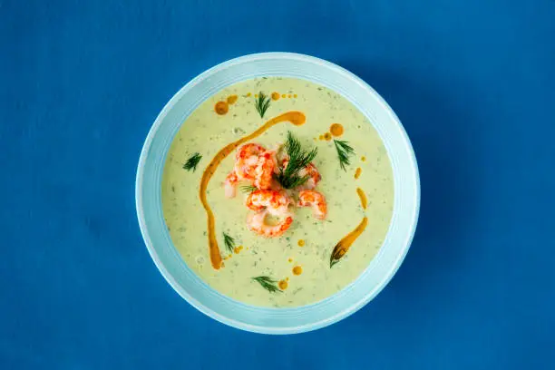 Chilled Cucumber and Crayfish Soup with dill on blue background with copy space.