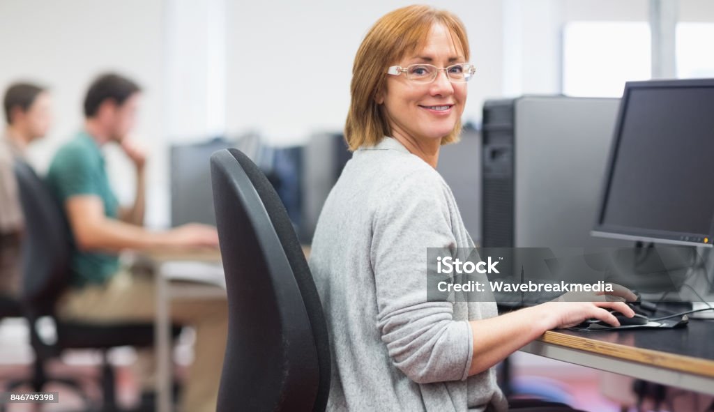 Mature students in the computer room Portrait of a smiling woman by other mature students using computers in the computer room Mature Adult Stock Photo