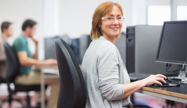 Mature students in the computer room Portrait of a smiling woman by other mature students using computers in the computer room middle age adult studying stock pictures, royalty-free photos & images