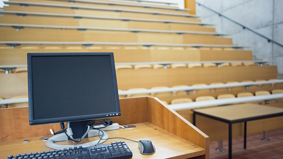 View of computer monitor with empty wooden seats with tables in a lecture hall