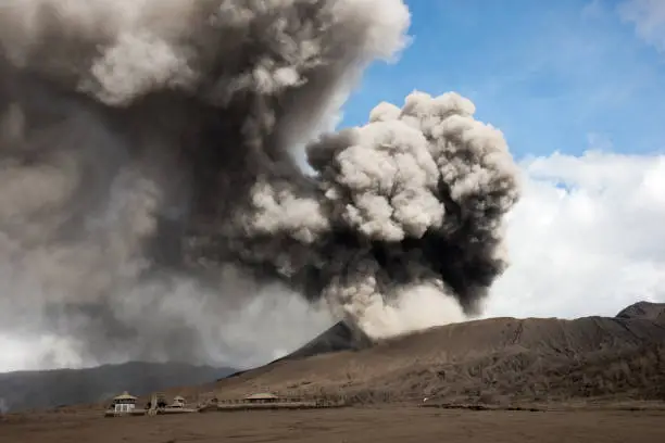 Grey smoke coming out of the active volcano mount Bromo filling the sky  with hindu temple in the valley at the Tengger Semeru National Park in East Java, Indonesia.