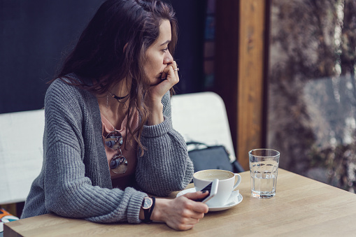 Mujer sentada sola, con café y mensajes de texto en su teléfono móvil photo