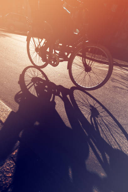 Shadow of unrecognizable cyclist riding a bike on road through city street in urban surrounding