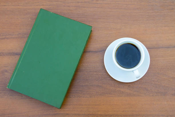 Cup of coffee and closed book on wooden table. Top view