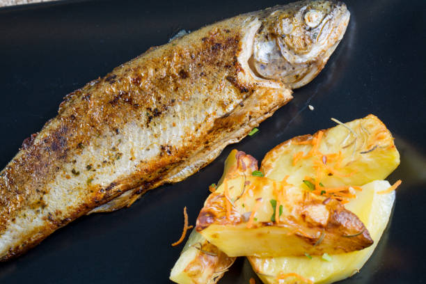 istock Close up of fresh fried trout with rustic potatoes on a black plate 846782336