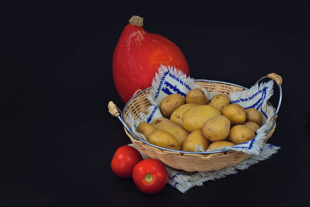 Organic potatoes in the basket, tomatoes and pumpkin on black back ground
