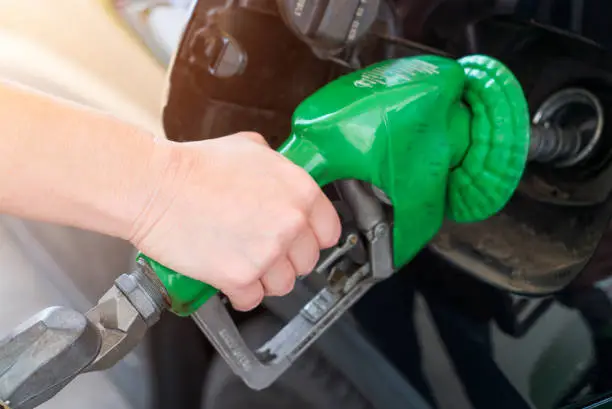 A female has her hand on a gas pump nozzle refueling her SUV at a American gas station.