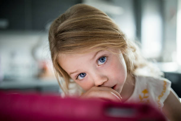 Little Girl with Big Blue Eyes Little girl sat in front of her pink digital tablet. Her big blue eyes peer over the top looking at the camera critical thinking kids stock pictures, royalty-free photos & images