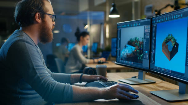 istock Creative Male Game Developer Works with Graphics for the New Level Design, He Sits at His Wooden Table Working on Two Display Personal Computer. Other People Work in This Creative Studio. 846843158