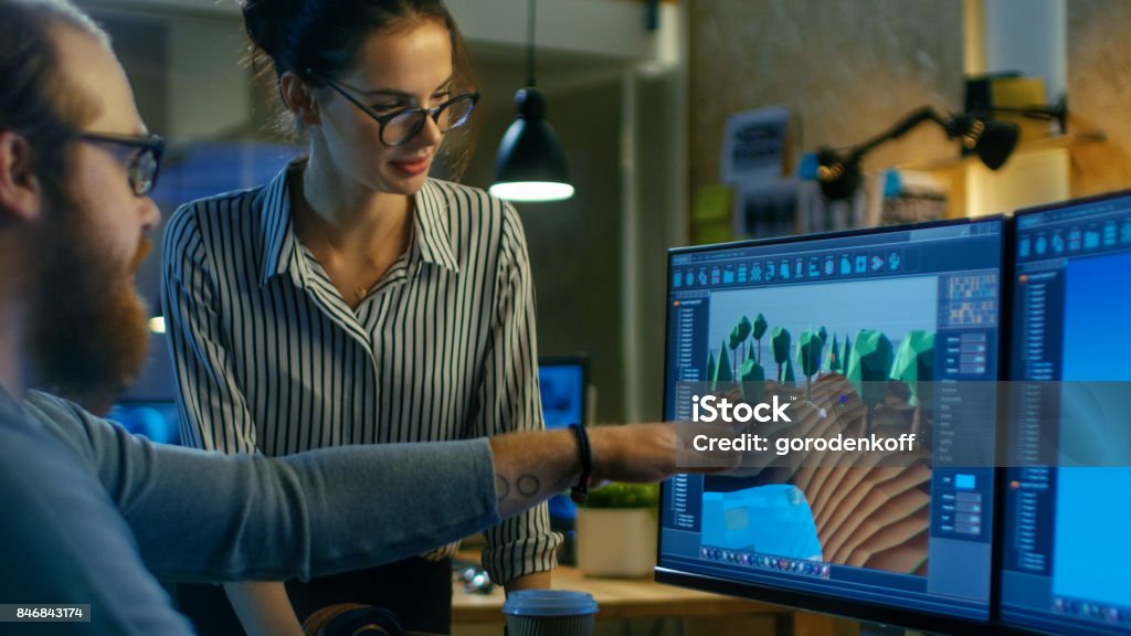 Male Game Developer Talks with Artistic Female Level Designer. Two Displays Show Totally Original Game. They Work in a Creative Office Loft. Design Professional Stock Photo