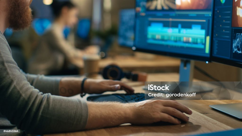 Male Videographer Edits and Cuts Footage and Sound on His Personal Computer with Two Displays. His Office is Modern and Creative Loft Studio. Working Stock Photo