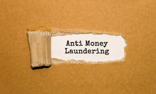Photo of The text Anti Money Laundering appearing behind torn brown paper