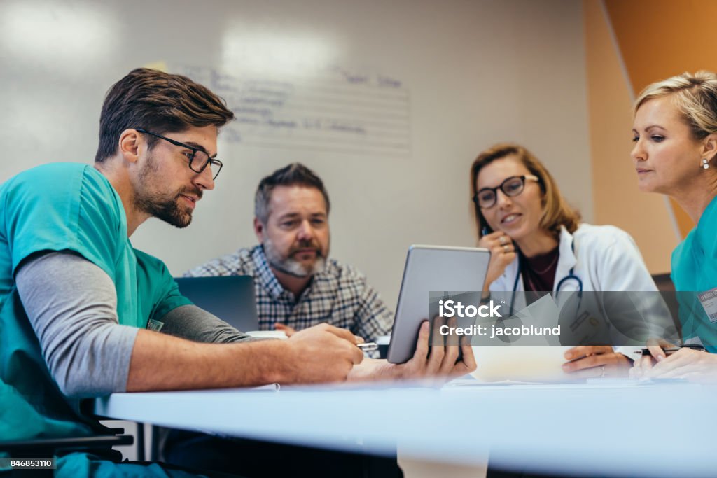 Medical staff having morning meeting in boardroom Team of medical staff having morning meeting in boardroom. Doctors and nurses looking at digital tablet. Healthcare And Medicine Stock Photo