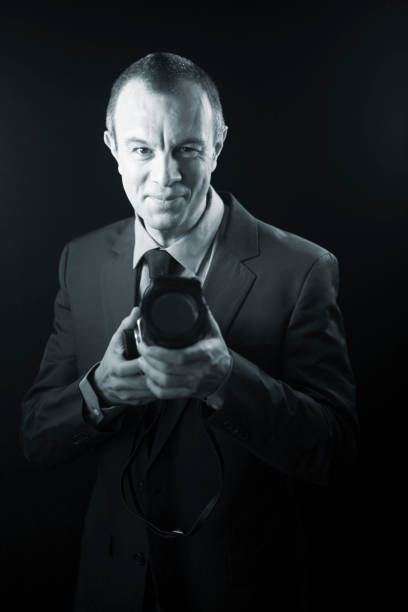 istock Photographer in studio in suit with camera aged in 40's against plain studio portrait background. 846874948