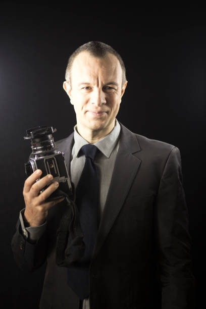 istock Photographer in studio in suit with camera aged in 40's against plain studio portrait background. 846874954