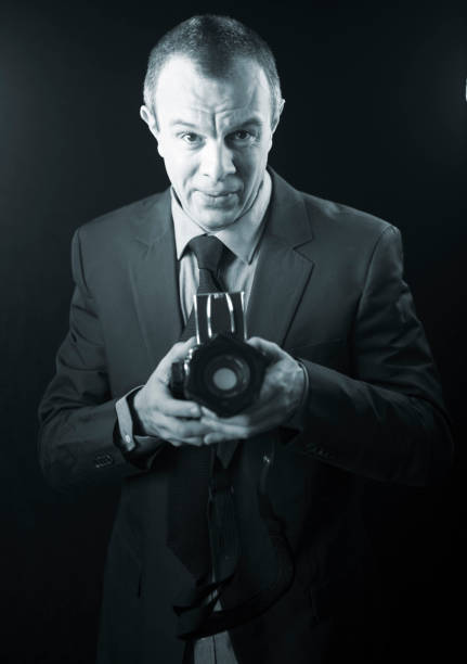 istock Photographer in studio in suit with camera aged in 40's against plain studio portrait background. 846874958