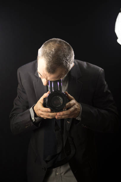 istock Photographer in studio in suit with camera aged in 40's against plain studio portrait background. 846874982