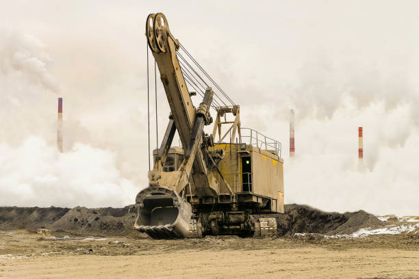 Big bucket mining excavator on a crawler track against a background of dense factory smog and fog with smoking chimneys. Heavy industry background. Excavator with mechanical drive and flexible suspension of work equipment. excavadora de minería cubo grande en un rastreador seguimiento contra un fondo de humo denso fábrica y niebla con chimeneas humeantes. fondo de industria pesada. excavadora con tracción mecánica y suspensión flexible del equipo de trabajo.