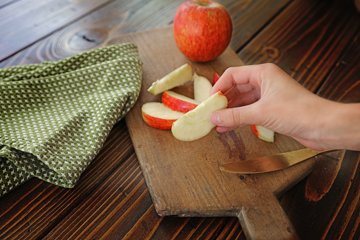 Red apple slices cut up on vintage cutting board with young hand grabbing slice