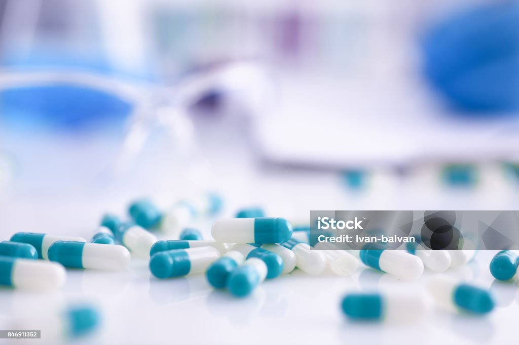 Tabletten, die verstreut auf dem Tisch des pharmazeutischen Labors - Lizenzfrei Medikamenten-Kapsel Stock-Foto