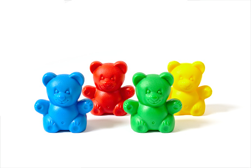 Small blue, red, yellow and green plastic toy bears isolated on white background arranged in two rows