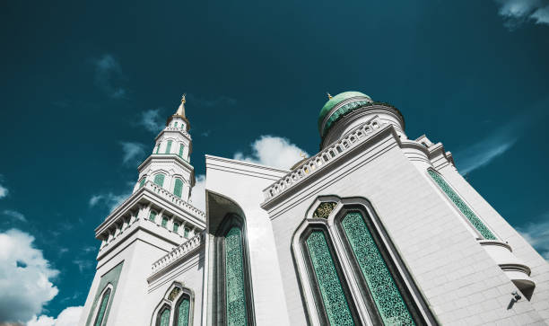 Side view from bottom of beautiful Grand Cathedral Mosque made of stone: teal fancy facade and golden spires, quotation from Quran, sunny autumn day, Moscow, Russia