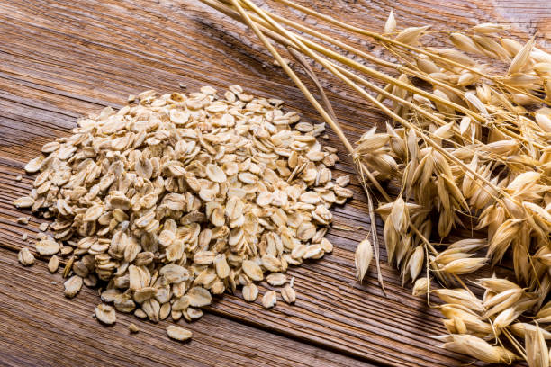 Corn spikes and oat flakes on a wooden background Pile of rolled oats and oat plant on beautiful garden table bran stock pictures, royalty-free photos & images