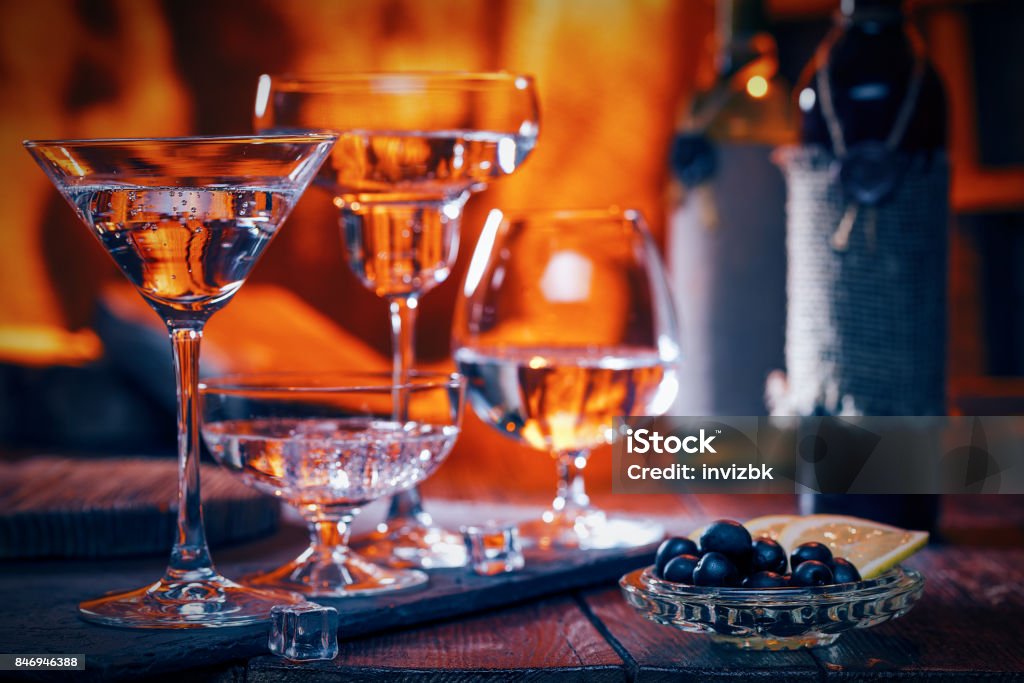 Cocktails near fireplace Liquids in various cocktail glasses in line. Olives and wine bottles on the table. Fire background Cocktail Stock Photo