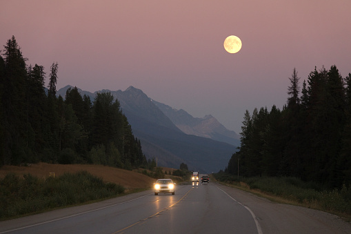 Traffic rolls by Red Pass on the Yellowhead Highway in British Columbia as a full harvest moon rises over the Rocky Mountains and Jasper National Park.