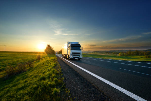 weißen lkw fahren auf der straße in die landschaft bei sonnenuntergang - vanishing point summer cloud sky stock-fotos und bilder