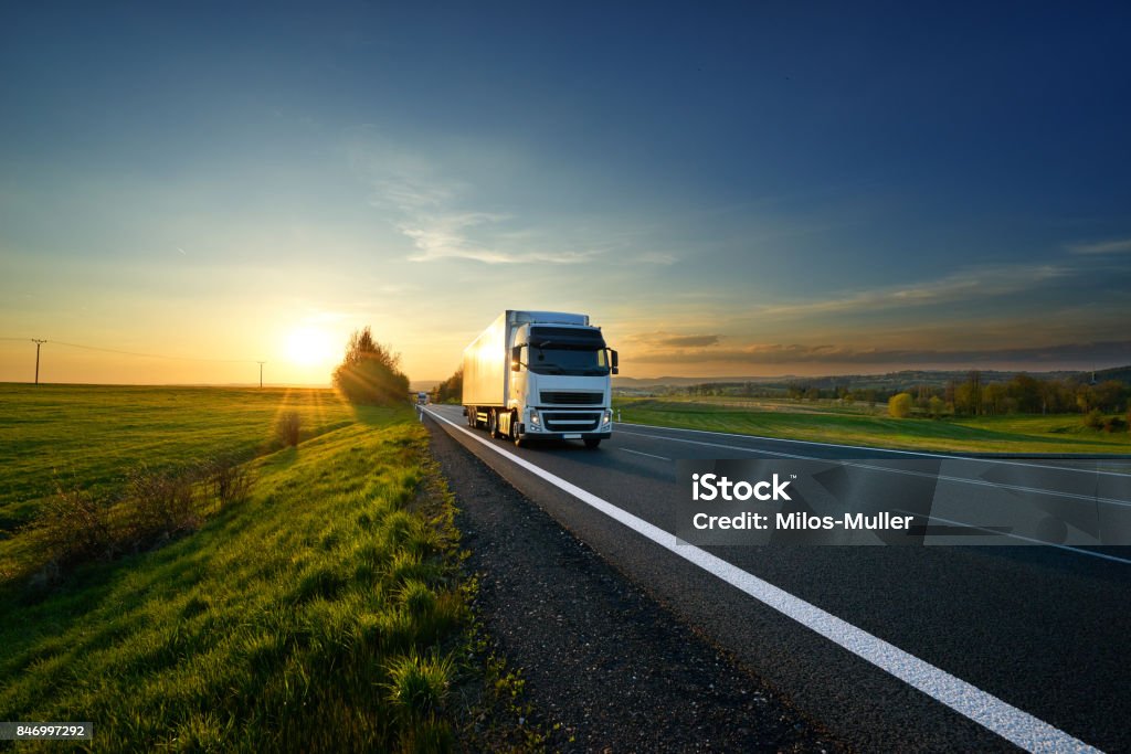 Camión blanco de conducción en la carretera en el paisaje al atardecer - Foto de stock de Camión de peso pesado libre de derechos