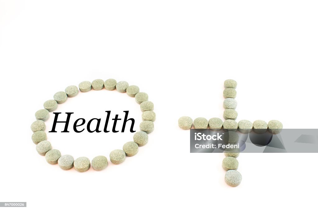 Circle, plus sign and spirulina pills. Contour of a circle and the plus sign made up of spirulina pills with word health. Supplement of vitamin B12. White background. 12th Century BC Stock Photo
