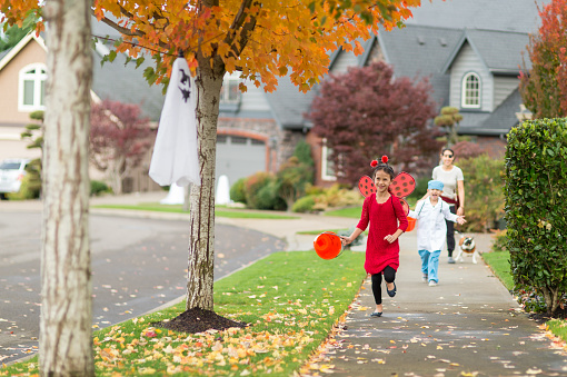 Ethnic children get a jump on Halloween trick or treating by going out in the afternoon in their neighborhood. She is dressed like a ladybug, he is dressed like a doctor in scrubs. They have their jack o' lantern buckets for collecting candy...