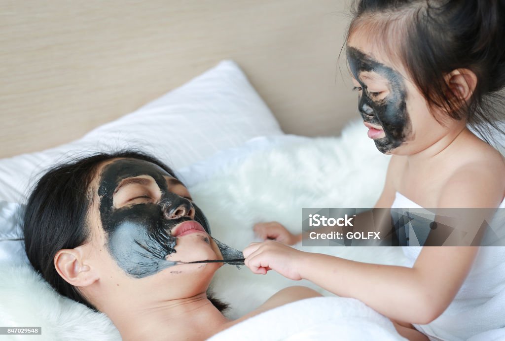 Child girl removed black mask from her mother, clean face. Facial Mask - Beauty Product Stock Photo