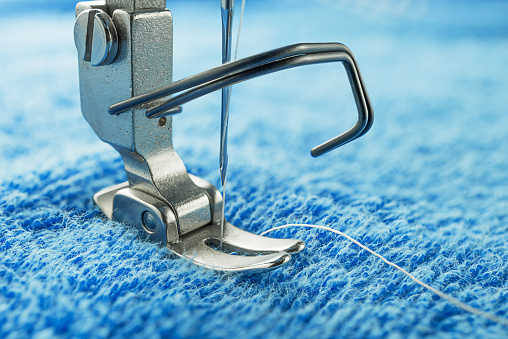 Macro image of sewing machine parts call presser foot and needle, on blue towel fabric